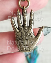 Load image into Gallery viewer, A gold-toned metal charm in the shape of a hand with detailed lines and symbols. The hand is a palmistry chart with astrological signs and symbols.