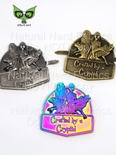 Load image into Gallery viewer, Three metal plate embellishments featuring a creature with a frog, an ape, and two humanoid figures. The plates are in different color schemes: antique silver, bronze, and rainbow. The text on the pins reads "Crafted by a Cryptid".
