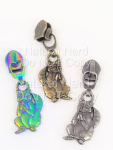 Load image into Gallery viewer, Three zipper pulls with a raccoon design. The zipper pulls are in three different finishes: antique brass, iridescent rainbow, and silver. Each zipper pull features a raccoon sitting with its paws clasped together.