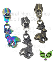 Load image into Gallery viewer, Three zipper pulls in the shape of a jackalope in three finishes: bronze, matte rainbow, and antique silver.