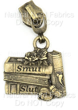 Load image into Gallery viewer, Antique Bronze zipper pull featuring a stack of books with the words "Smut" and "Slut" on the spines. The design includes a rose and a book with a chili pepper. A metal ring connects the pull to the zipper.