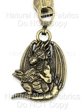 Load image into Gallery viewer, A bronze-toned metal zipper pull featuring a dragon wearing glasses and reading a book. The dragon has wings and a long tail.
