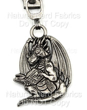 Load image into Gallery viewer, A silver-toned metal zipper pull featuring a dragon wearing glasses and reading a book. The dragon has wings and a long tail.