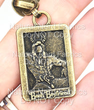Load image into Gallery viewer, A rectangular, bronze-colored zipper pull with a detailed relief of a horned man. The pendant has the words "Book Boyfriend" in a stylized font at the bottom.