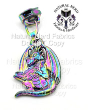 Load image into Gallery viewer, A matte rainbow-toned metal zipper pull featuring a dragon wearing glasses and reading a book. The dragon has wings and a long tail.
