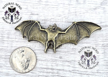Load image into Gallery viewer, A bronze-colored metal bat-shaped snap with outstretched wings. The bat is detailed with textured wings and body. The image includes a quarter for size comparison.
