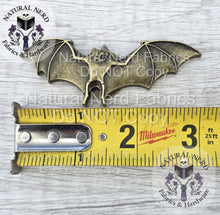 Load image into Gallery viewer, A bronze-colored metal bat-shaped snap with outstretched wings. The bat is approximately 3 inches wide. A yellow measuring tape is placed below the bat.