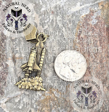 Load image into Gallery viewer, An bronze detailed zipper pull designed to look like a launching space shuttle shown next to a quarter for scale.