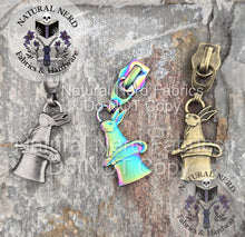 Load image into Gallery viewer, Three rabbit-in-a-hat zipper pulls on a stone surface with 'Natural Nerd' branding. Colors shown are antique nickel, matte rainbow, and bronze.