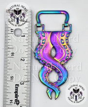 Load image into Gallery viewer, An iridescent, metallic, octopus-tentacle-shaped strap anchor next to a ruler for scale on a white background. The product features a holographic rainbow finish with blue, purple, and green tones. The ruler shows the product is approximately 3.75 inches long.