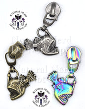 Load image into Gallery viewer, Three zipper pulls with an angler fish design. Shown in antique nickel, bronze, and matte rainbow finishes.