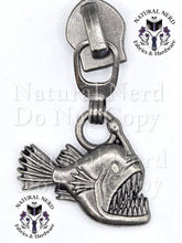 Load image into Gallery viewer, An antiqued silver metal angler fish zipper pull with a wide-open mouth showing sharp teeth. The image features 'Natural Nerd Fabrics & Hardware' watermarks on a white background.