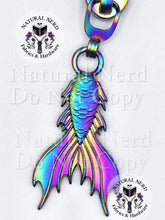 Load image into Gallery viewer, A matte rainbow metal mermaid tail zipper pull next, with a 'Natural Nerd Fabrics & Hardware' logo watermark on the image.