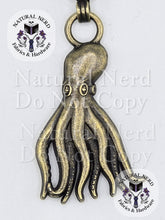Load image into Gallery viewer, A bronze metal octopus zipper pull with detailed tentacles and suction cup patterns, shown on a white background with 'Natural Nerd Fabrics & Hardware' watermarks.
