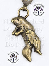 Load image into Gallery viewer, close up of a bronze zipper pull with a momma and baby manatee design
