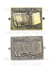 Load image into Gallery viewer, Two antique-style metal bookbinding plates, one bronze and one silver, with the text "Bound By Hand". The plates are about 2 inches wide and feature a detailed image of a book being bound.
