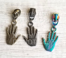 Load image into Gallery viewer, Three zipper pulls with a palm reading design. The pulls are in antique gold, antique nickel, and iridescent blue.
