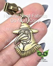 Load image into Gallery viewer, Bronze metal zipper pull featuring a plague doctor with a long beak, wearing a hat and goggles. 
