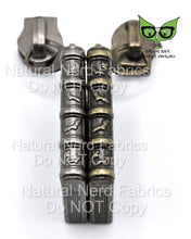 Load image into Gallery viewer, Two antique-style book-shaped zipper pulls, one silver and one gold, with a bat design. The zipper pulls are on a white background and the spines of the books are facing up and feature a bat motif.
