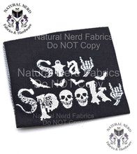 Load image into Gallery viewer,  Black fabric label with white text and graphics. The words "Stay Spooky" are displayed with a ghost, bats, skulls, and skeleton hand graphics. The label also includes the text "Natural Nerd Fabrics Do NOT Copy" as a watermark.
