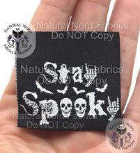 Load image into Gallery viewer, Black fabric label with white text that reads "Stay Spooky" with bat and skull graphics. The label also has the text "Natural Nerd Fabrics" and "Do NOT Copy" as a watermark. Label is shown held in a hand for scale reference.
