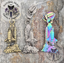 Load image into Gallery viewer, A collection of three detailed zipper pulls designed to look like a launching space shuttle. Three finishes are on display: matte rainbow, antique silver, and bronze.
