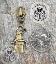 Load image into Gallery viewer, Bronze rabbit-in-a-hat zipper pull on a stone surface with 'Natural Nerd' branding shown next to a US quarter coin for size comparison.
