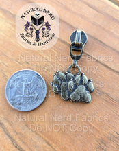 Load image into Gallery viewer, An bronze detailed zipper pull designed to look like a pair of canine paw prints shown next to a quarter for scale. 
