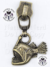 Load image into Gallery viewer, An antiqued bronze metal angler fish zipper pull with a wide-open mouth showing sharp teeth. The image features 'Natural Nerd Fabrics &amp; Hardware' watermarks on a white background.

