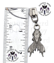 Load image into Gallery viewer, A silver-toned metal mermaid tail zipper pull next to a metal ruler for scale, with a 'Natural Nerd Fabrics &amp; Hardware' logo watermark on the image.
