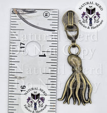 Load image into Gallery viewer, An antique bronze octopus zipper pull shown next to a metal ruler for scale, with a circular 'Natural Nerd Fabrics &amp; Hardware' logo sticker on the right.
