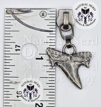 Load image into Gallery viewer, An antiqued silver shark tooth zipper pull next to a metal ruler for scale, with two circular 'Natural Nerd Fabrics &amp; Hardware' brand stickers on the background.
