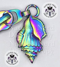 Load image into Gallery viewer, A matte rainbow seashell-shaped metal zipper pull, shown on a white background with 'Natural Nerd Fabrics &amp; Hardware' watermarks.
