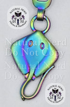 Load image into Gallery viewer, A rainbow-toned metal zipper pull shaped like a stingray, featuring detailed eye and mouth carvings, shown against a white background with 'Natural Nerd Fabrics &amp; Hardware' watermarks.
