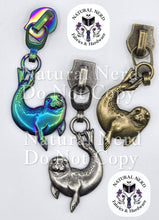 Load image into Gallery viewer, Three seal-shaped zipper pulls in different finishes (matte rainbow, antique silver, and bronze) on a white background with 'Natural Nerd Fabrics &amp; Hardware' logos and a 'Natural Nerd Do Not Copy' watermark.
