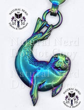 Load image into Gallery viewer, An iridescent metallic seal zipper pull with a holographic finish shifting between green, blue, and purple, shown on a white background with 'Natural Nerd Fabrics &amp; Hardware' watermarks.
