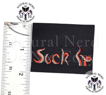 Load image into Gallery viewer, A square black fabric patch with the word 'Suck It' embroidered in red and white, shown next to a ruler for scale on a white background. Watermarks for 'Natural Nerd Fabrics &amp; Hardware' are visible.
